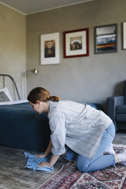 A professional cleaner from Arkley Carpet Cleaners dressed in a white protective suit, mask, and gloves, using a carpet cleaning machine to deep clean a beige, textured carpet in a modern residential 