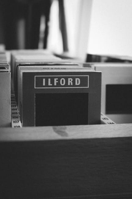 Close-up of an office desk drawer containing neatly organized folders and documents, with a visible label reading 'ILFORD' on one of the folders. The surface of the desk is smooth and appears clean, r